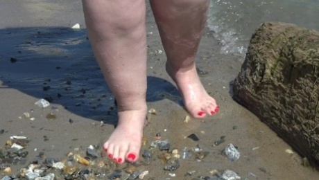 Fat bare legs with red pedicure walk along the bank of the river, fetish.